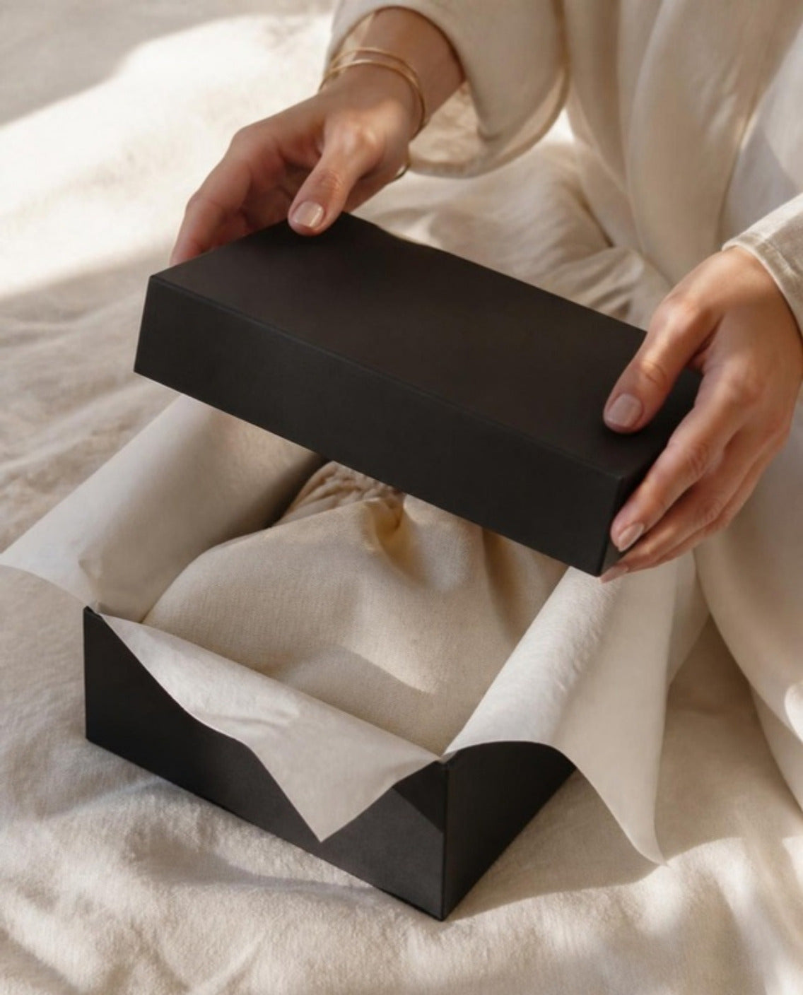 Hands lifting the lid of a black gift box lined with tissue paper